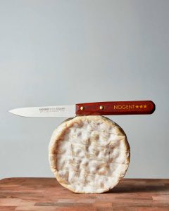 Nogent iconinc paring knife resting on a wheel of cheese